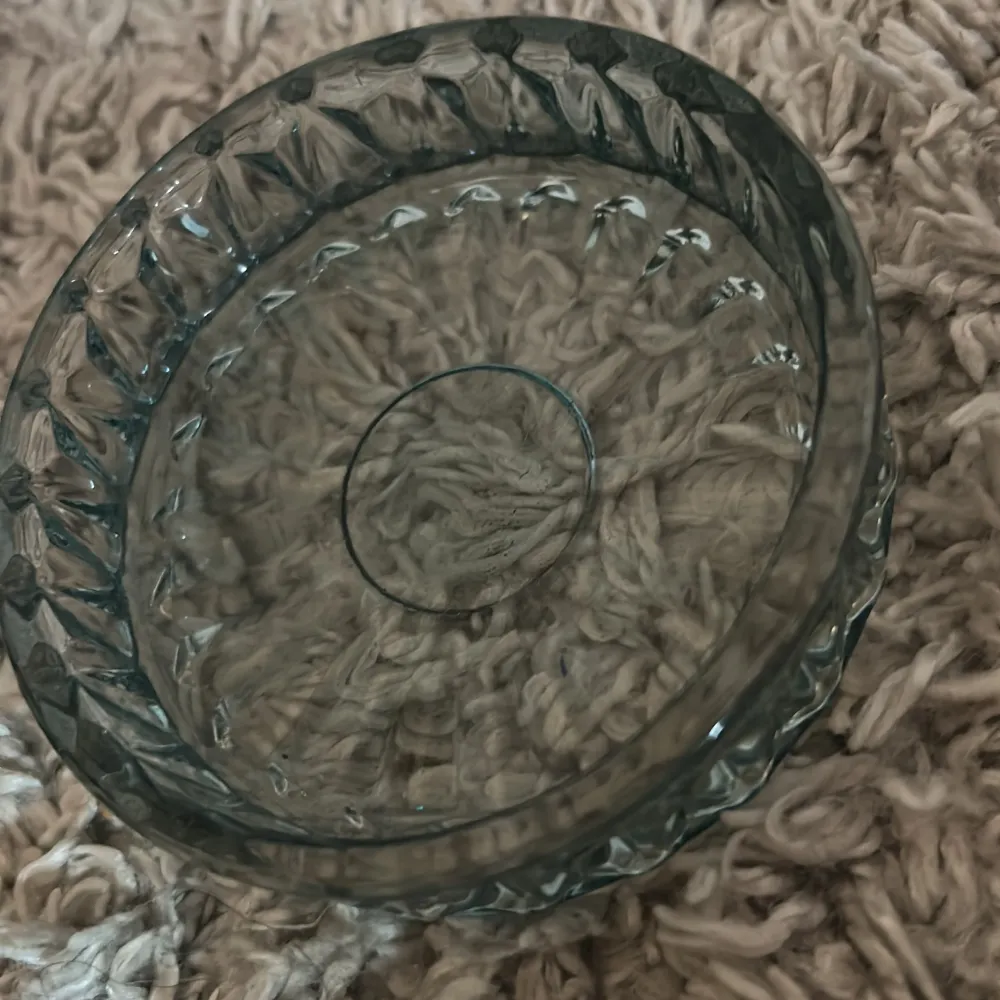 Säljer en rund liten skål i tjockt, transparent glas med dekorativt slipat mönster runt kanterna. Perfekt som smyckesfat eller förvaring av små accessoarer. Klassisk och stilren design.. Asusteet.
