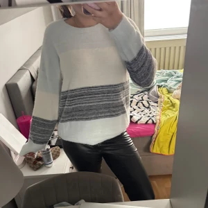 Vit och grå stickad tröja - Mysig stickad tröja i vitt och grått med breda horisontella ränder. Tröjan har rund halsringning och långa ärmar. Perfekt för kyligare dagar och enkel att matcha med olika outfits.