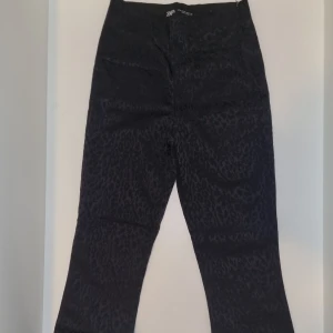 Svarta leopardmönstrade byxor från Zara - Säljer ett par svarta byxor från Zara i storlek XS med diskret leopardmönster. Byxorna har hög midja och utsvängda ben, vilket ger en snygg och modern siluett. Perfekta för dig som vill ha något extra i garderoben. Tveka inte att höra av dig vid frågor eller bilder!