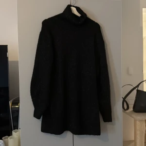 Svart glittrig polotröja/klänning  från H&M - Säljer en svart glittrig polotröja från H&M. Tröjan har lång ärm och är stickad med ett glansigt garn som ger en festlig känsla. Perfekt för dig som vill sticka ut lite extra. Polokrage och normal passform. Den kan användas som klänning då den är lite längre. 