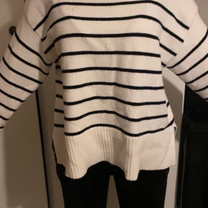 Vit och svart randig stickad tröja - Säljer en vit stickad tröja med svarta horisontella ränder. Tröjan har lång ärm, rund halsringning och bred ribbad kant nedtill. Perfekt för en avslappnad och stilren look.