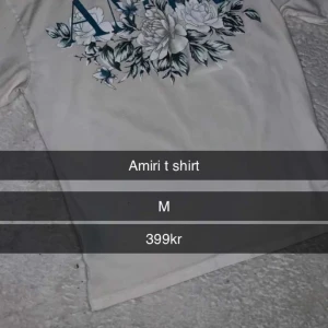 Vit t-shirt med blommigt tryck från Amiri - Vit t-shirt från Amiri med stort blommigt tryck och blå bokstäver på framsidan. Klassisk passform och korta ärmar. Perfekt för dig som gillar stilrena plagg med en twist.
