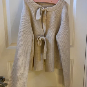 Beige stickad kofta med knyt från OBJECT - Säljer en beige stickad kofta från OBJECT med långa ärmar och två knytband framtill. Koftan har en mjuk och ribbad struktur, perfekt för lager på lager. Enkel och stilren design som passar till mycket. Storlek L men sitter som XS eller S.