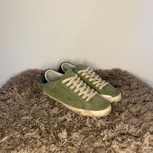 Golden Goose Sneaker - Snygga gröna sneakers från Golden Goose med vit sula och vita snören. Skorna har svart detalj på hälen och är tillverkade i mocka. Perfekta för dig som vill ha en stilren och trendig look. Passar perfekt för sommaren! 