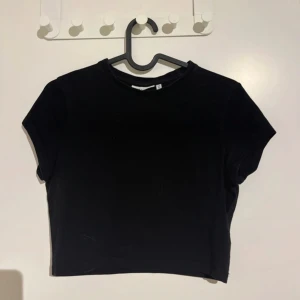 Svart croppad t-shirt från Weekday - En enkel svart croppad t-shirt från Weekday med rund halsringning och korta ärmar. Perfekt basplagg som passar till mycket och har en stilren look.