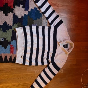 Randig stickad tröja från Hampton Republic - Säljer en vit och marinblå stickad tröja från Hampton Republic. Tröjan har breda horisontella ränder, lång ärm och ribbade muddar. Perfekt för en klassisk och avslappnad stil.