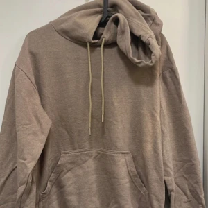 Beige hoodie med ficka - Säljer en enkel beige hoodie med huva och dragsnören. Tröjan har en stor magficka och långa ärmar. Perfekt för en avslappnad stil och passar året runt.