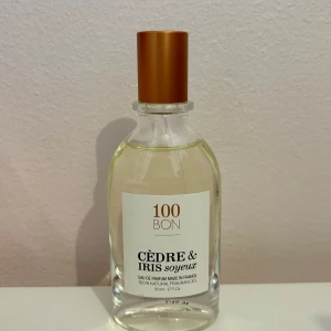 Cèdre & Iris Soyeux Eau de Parfum från 100BON - En elegant parfym med noter av cederträ och iris. Flaskan är genomskinlig med en stilren etikett och har ett kopparfärgat lock. Parfymen är tillverkad i Frankrike och innehåller 100% naturliga doftämnen.