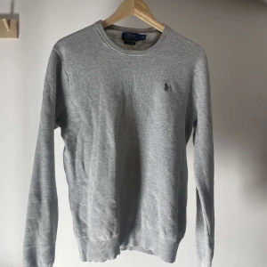 Ljusgrå tröja från Polo Ralph Lauren - Säljer en ljusgrå långärmad tröja från Polo Ralph Lauren i bomull. Tröjan har rund halsringning och den klassiska broderade loggan på bröstet. Perfekt för en stilren och enkel look.