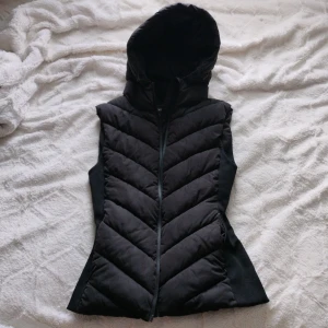 Svart väst med luva från Zara💕 - Hej, Säljer en snygg svart väst från Zara med luva och dragkedja framtill. Västen har en figurnära passform och är vadderad med snygga sömmar i ett V-mönster. Perfekt nu på våren för att ha över en hoodie eller tröja när det är lite kyligt ute.❤️ Använd fåtal gånger utan skråmor. Säljer västen då jag inte passar den längre❣️