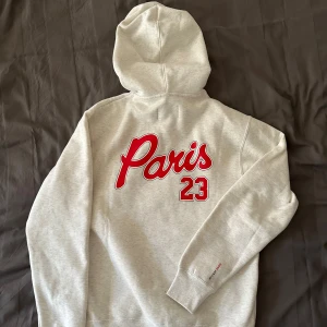 Grå hoodie Paris Saint-Germain x Jordan - Säljer en helt oanvänd ljusgrå hoodie från Jordan i samarbete med Paris Saint-Germain. Tröjan har röd Paris-tryck och siffran 23 på ryggen samt en liten logga och text på bröstet. Klassisk känguruficka och huva med dragsko. Stor i storlek är som en medium. 