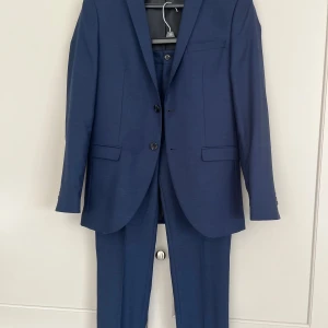 Blå kostym stl 46 ålder 14/15 år nyskick - Kostym från Jack & Jones JPRSOLARIS SUPER SLIM FIT stl 46 på både byxa och kavaj. Passade vår son när han var 14/15 år. Färg: BLÅ / DARK NAVY. Snyggt tyg med struktur. Pris: 1000:- Endast använd två gånger. NYSKICK. Djur- och rökfritt hem.