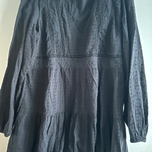 Svart klänning med v-ringning från Zara - Säljer en svart klänning med v-ringning och långa ärmar. Klänningen har broderade detaljer och en lätt volang nedtill. Perfekt för dig som gillar en bohemisk och avslappnad stil.