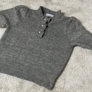 Grå stickad tröja från Holly & Whyte - Mysig grå stickad tröja från Holly & Whyte med pärlknappar framtill och diskret glittrigt garn. Tröjan har lång ärm, ribbade muddar och en fin strukturstickning. Skriv för bild på💗