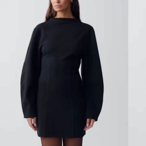 Figursydd svart långärmad kortklänning - Svart kortklänning med lång ärm och hög hals. Klänningen har en figursydd passform och är tillverkad i ett slätt material. Helt ny!