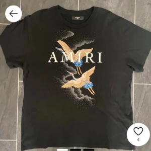 Svart t-shirt med tryck från Amiri - Säljer en svart t-shirt från Amiri med stort tryck av två tranor och vita bokstäver på bröstet. T-shirten har rund hals och korta ärmar. Perfekt för dig som gillar streetwear och snygga prints.