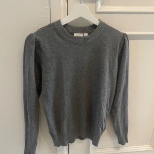 Grå stickad tröja från Saint Tropez - Mysig grå stickad tröja från Saint Tropez med rund halsringning och långa ärmar. Tröjan har ribbade muddar vid ärmslut och nederkant, vilket ger en klassisk och stilren look. 