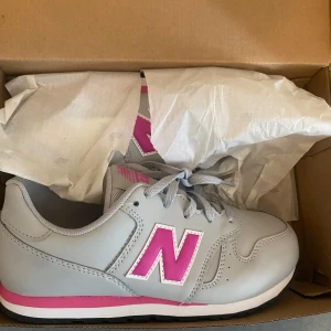 Grå New Balance sneakers med rosa detaljer - Säljer ett par grå New Balance sneakers med rosa och vita detaljer. Skorna är helt nya i kartongen aldrig använda i storlek 36! 