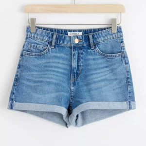 Low waist jeansshorts från Lindex - Säljer ett par klassiska blå jeansshorts från Lindex. De har en snygg upprullad kant och en knapp i midjan. Perfekta för sommardagar! 💙