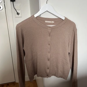 Beige ribbad kofta från 157 - Säljer en beige ribbad kofta från Lager 157 i storlek M. Koftan har långa ärmar, rund halsringning och knäppning framtill med små knappar. Perfekt att slänga över en topp eller klänning för en snygg lager-på-lager-look.