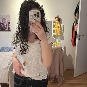 Vit spetsblus med broderade detaljer - Säljer en vit blus med spets och broderade detaljer. Blusen har korta ärmar och ett vackert mönster med genombrutna partier. Perfekt för dig som vill ha en romantisk och luftig topp till sommaren.