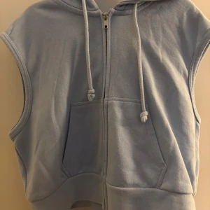 Ljusblå ärmlös hoodieväst från Divided - Säljer en ljusblå hoodieväst från Divided H&M. Västen har dragkedja framtill, två fickor och huva med dragsko. Perfekt för lager-på-lager och en sportig look. Det är 2 samma hoodie väst fast en är i storlek XS och den andra i M