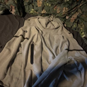 Ljusgrå hoodie från Nike med svarta detaljer -  Dragkedja  är trasig men funkar som ny finns ett hål men de syns inte