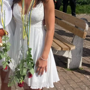 Vit klänning - Hej💕Säljer nu en söt vit klänning med spetsdetaljer och v-ringad urringning. Super fin öppen i ryggen, med smala axelband som korsas i ryggen och knyts för en justerbar passform. Passar till studenten eller annan skolavslutning☀️  Använd endast en gång, så den är i nyskick o inga fläckar. Hör av er vid frågor!