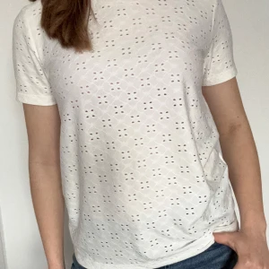 Vit broderad t-shirt - Säljer en vit t-shirt från Jacqueline de Yong med broderat hålmönster över hela plagget. Endast använd några enstaka gånger. Perfekt för en fräsch och stilren look!