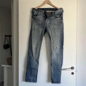 Slim fit jeans från &Denim - Säljer ett par blå slim fit jeans från &Denim med klassisk femficksdesign och knappar i gylfen. Jeansen har en snygg tvättad look med lätt slitna detaljer och raka ben. Perfekta för dig som gillar en smalare passform.