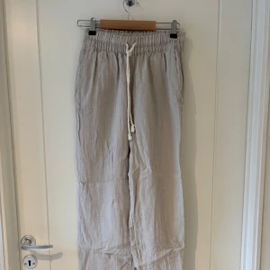 Beiga linnebyxor - Säljer ett par ljusbeiga linnebyxor från H&M med bred resår i midjan och vit snörning framtill. Byxorna har raka ben och avslappnad passform, perfekta för varma dagar nu i sommar! De kan även bäras som både hög- och lågmidjat och är relativt korta i benen 💕