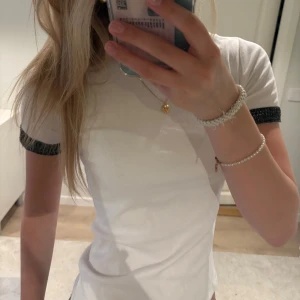 Vit t-shirt med svarta detaljer - Säljer en vit t-shirt från Zara med snygga svarta och guld virkade detaljer på ärmen. T-shirten har en klassisk passform och är tillverkad i mjuk bomull. Perfekt för en stilren och trendig look.