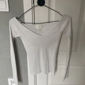 Vit ribbad långärmad topp från H&M - Säljer en vit ribbad långärmad topp från H&M. Toppen har v-ringning och är figurnära med stretchigt material. Perfekt att styla med jeans eller kjol för en enkel och snygg look.