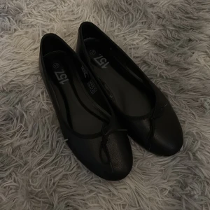 Svarta ballerinaskor - Klassiska svarta ballerinaskor från lager 157 med rund tå och en liten rosett framtill. Skorna har en platt sula och är tillverkade i syntetmaterial. Perfekta för en stilren och enkel look. Skorna är aldrig använda enbart testade och säljer pågrund av att jag beställde fel storlek! Säljer i storlek 38.