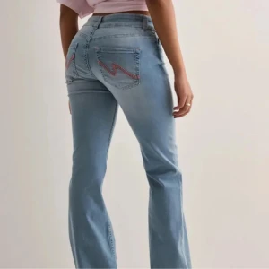 Ljusblå bootcut jeans med broderade bakfickor - Säljer ett par ljusblå jeans med bootcut passform och snygga broderade detaljer på bakfickorna. Säljer då de är för stora för mig! Använda en gång!