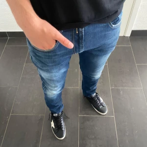 Replay anbass  - Säljer ett par snygga blå jeans från Replay i modellen slim fit. Jeansen har klassisk femficksdesign, dragkedjegylf och coola slitningar på låren. Perfekta för dig som gillar en modern och stilren look.