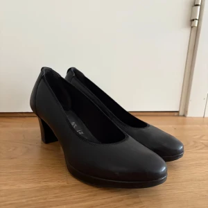 Svarta klassiska pumps i skinn - Stilrena svarta pumps med rund tå och låg klack. Endast använda en gång då de inte passade mig. Mycket bekväma och sitter åt bra. Nypris 1000kr