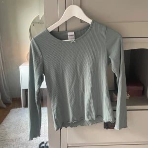 Ljusgrön ribbad pyjamas tröja  - Säljer en ljusgrön långärmad tröja från Kappahl med ribbad struktur och liten rosett vid halsen. Tröjan har en rund halsringning och vågig kant vid ärmslut och nederkant. Perfekt för dig som gillar enkel och stilren look.