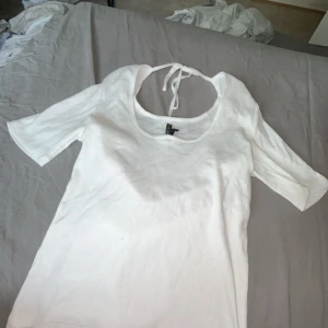 Vit ribbad topp med knyt i nacken - Vit ribbad topp med kort ärm och snygg djup urringning. Knytband i nacken ger en extra detalj och gör toppen lite mer unik. Perfekt till jeans eller kjol för en clean look.