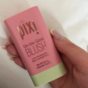 Pixi On-the-Glow Blush stick - Säljer en Pixi On-the-Glow Blush i stickformat. Färgen är en fräsch rosa nyans som ger kinderna ett naturligt glow. Förpackningen är rosa med ljusgrön botten och innehåller 19 g. Perfekt att ha med i väskan för snabba touch-ups.