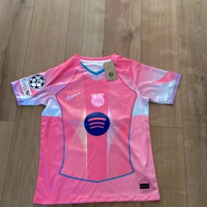 Barça Lamine Yamal rosa fotbollströja Nike M - Snygg FC Barcelona fotbollströja i rosa och ljusblått med Lamine Yamal och nummer 10 på ryggen. Nike-logga, klubbmärke och Spotify-sponsor på bröstet. Kortärmad modell i lätt, ventilerande material. Champions League-märke på ärmen.