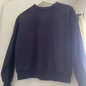 Mörkblå sweatshirt från Gina Tricot - Säljer en mörkblå sweatshirt från Gina Tricot med texten 'AMOUR' i små prickar framtill. Tröjan har rund hals, ribbade muddar och lång ärm. Perfekt för dig som gillar enkel stil med en liten twist. Materialet är mjuk bomull och polyester.