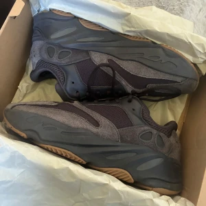 Adidas Yeezy Boost 700 Utility black  - Säljer ett par Adidas Yeezy Boost 700 i mörkgrå färg med bruna detaljer på sulan. Skorna har en chunky siluett, mesh och mocka-paneler, samt snörning. Snygg retrovibe och riktigt bekväma med Boost-dämpning. Perfekt för dig som gillar streetwear och vill sticka ut. Små repor på sulan men inget märkvärdigt 