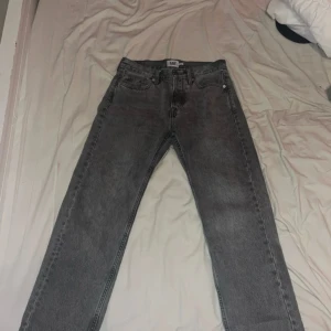 Lager 157 jeans straight fit - Säljer ett par grå lager 157 jeans med klassisk knappgylf och raka ben. Jeansen har fem fickor och är i ett snyggt tvättat grått denimtyg. Perfekta för dig som gillar en tidlös och clean look.