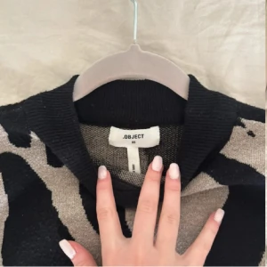 Beige och svart zebramönstrad tröja Object - Säljer en snygg stickad tröja från Object i storlek XS. Tröjan har ett coolt zebramönster i beige och svart, med hög hals och långa ärmar. 