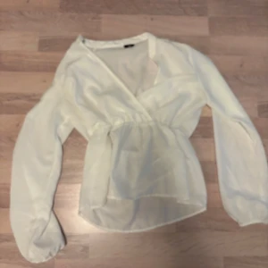 Vit blus - Säljer en superfin vit omlottblus från Vero Moda i storlek XS. Blusen har långa ärmar, markerad midja och är gjord i ett lätt, transparent tyg som ger en luftig känsla. Perfekt för dig som gillar en feminin och stilren look.
