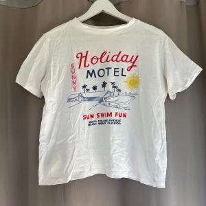 Vit Holiday Motel t-shirt från H&M - Vit t-shirt från H&M med färgglatt tryck. Har två små fläckar på magen men syns inte så mycket