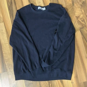 Mörkblå sweatshirt från Stone Island - Säljer en mörkblå sweatshirt från Stone Island med klassisk rund hals och ribbade muddar. Tröjan har den ikoniska Stone Island-patchen på vänster ärm med broderad kompass i gult och grönt.
