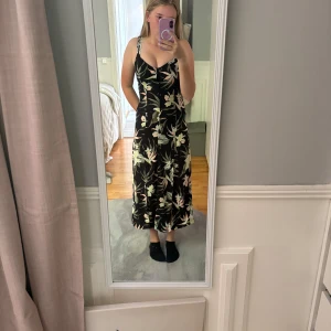 Svart blommig långklänning - Supersnygg svart långklänning med blommor och knappar famtill.