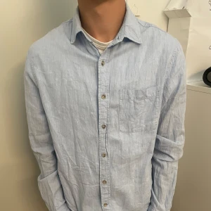 Ljusblå linneskjorta från Dressmann - Säljer en stilren ljusblå skjorta från Dressmann i linnemix. Skjortan har klassisk krage, bröstficka och knäppning framtill. Perfekt för en chill och fräsch look under varmare dagar.